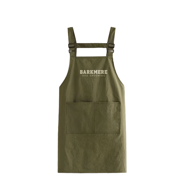 Olive green Barkmere grooming apron with cross-back straps and a large twin front pocket, shown flat